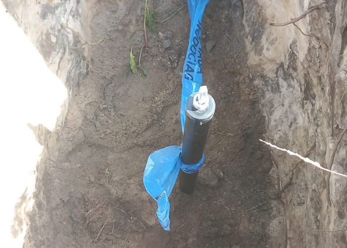 Rura owinięta taśmą w wykopie z kablami.