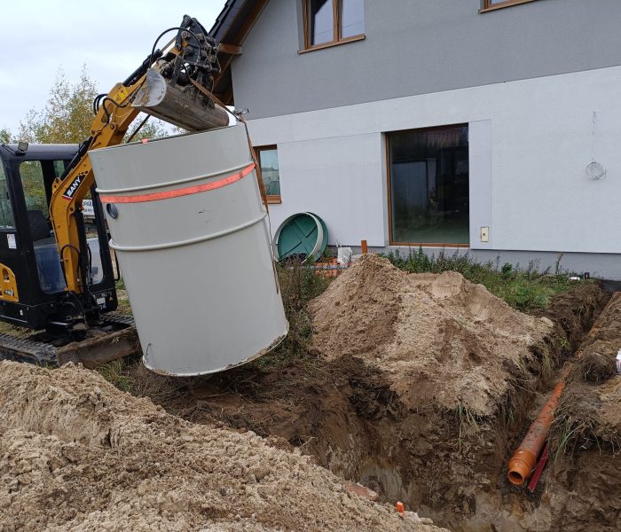 Koparka umieszczająca betonowy zbiornik w wykopie obok domu.